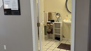 A hallway leading to a bathroom with a tiled floor, a white sink, and a mirror.