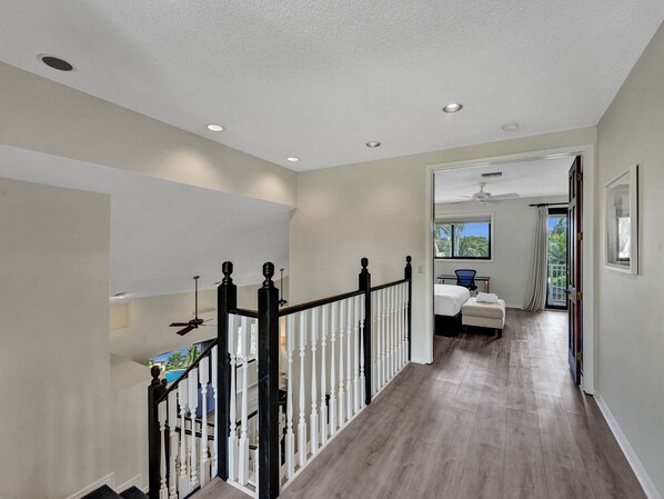 A spacious hallway with a wooden staircase, a ceiling fan, and a view of a bedroom with a bed and a window. - Waterfront Heated Saltwater Pool & Kayaks (Wilton Manors)