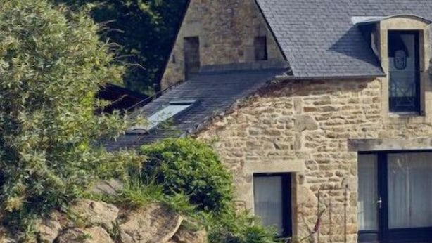 Une maison en pierre avec un toit en pente, une cheminée et un petit porche.