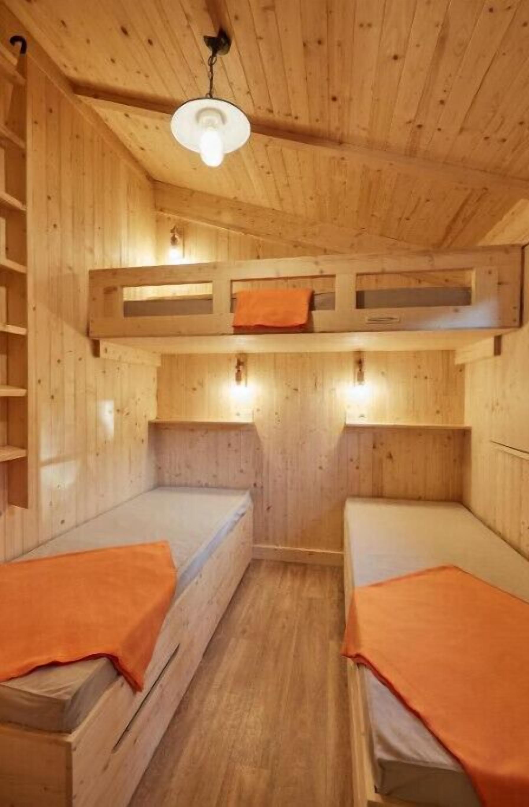 A wooden cabin with two bunk beds, a wooden ceiling, and a single light fixture.