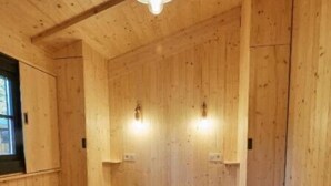 Une pièce de style cabane en bois, avec un lit, un luminaire suspendu et deux lampes fixées au mur.