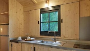 L’intérieur d’un chalet en bois comprend un coin cuisine équipé de placards, d’un évier et d’une fenêtre donnant sur un paysage verdoyant.