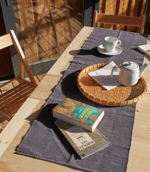 Ein Holztisch mit einer gewobenen Tischmatte, ein Buch mit dem Titel 'LOOSE BONDS', ein Teekessel und eine Tasse auf einem Untertasse.