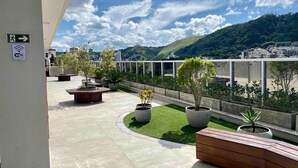 Terraza en la azotea con vistas a una colina verde, plantas en macetas y un banco de madera.