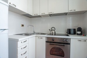 A modern kitchen with white cabinets, a stainless steel sink, a kettle, a coffee maker, and an oven. - Casa Novecento Prati (Roma)