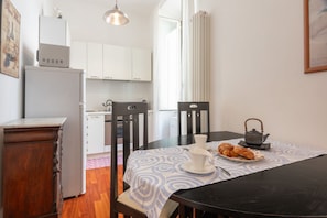A dining area with a table set for two, a kettle, and a plate of croissants.