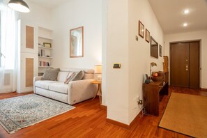 Un salon avec un canapé, un tapis, une bibliothèque et une porte.