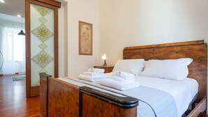 A bedroom with a wooden bed, a nightstand with a lamp, and a wall with a decorative panel and a framed picture. - Casa Novecento Prati (Roma)