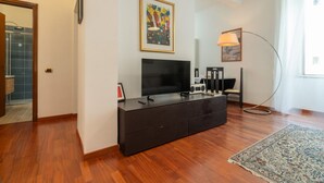 Un salon moderne avec un téléviseur à écran plat, un meuble en bois foncé, une lampe sur pied et un tapis à motifs.