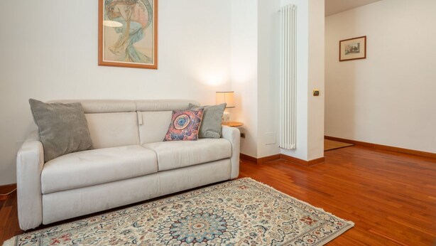 A living room with a sofa, a patterned rug, a lamp, and a framed picture on the wall. - Casa Novecento Prati (Roma)