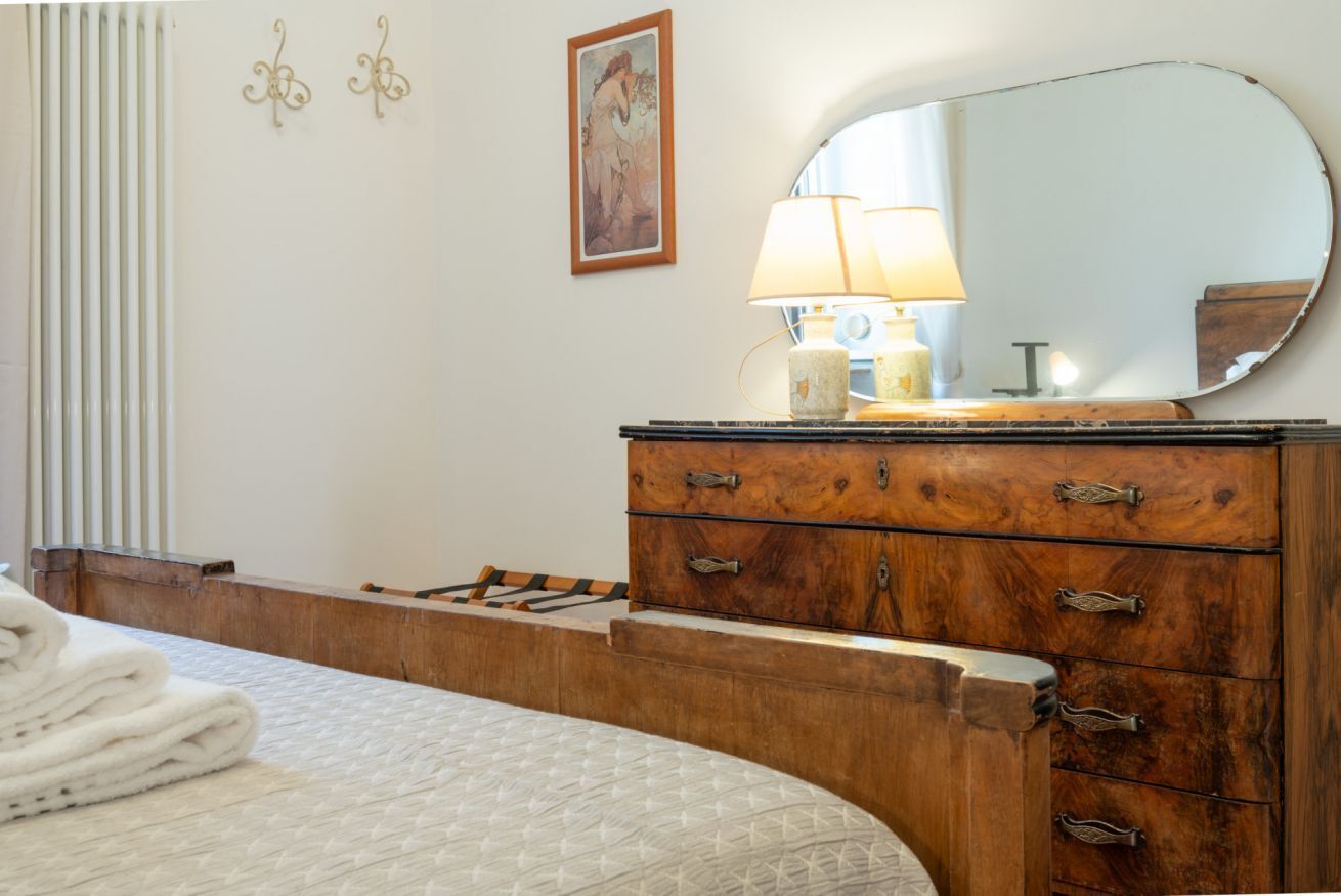 A bedroom with a bed, a wooden dresser, a mirror, a lamp, and a framed picture on the wall.
