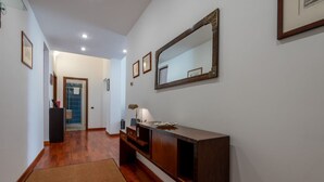 A hallway with a wooden floor, a dark wooden console table, a mirror, and framed pictures on the wall. - Casa Novecento Prati (Roma)