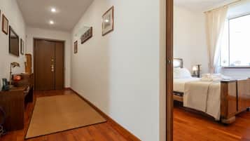 Ein Hotelzimmer mit Holzboden, einem Bett mit weißer Bettdecke, einem Nachttisch mit Lampe und einem Fenster mit Vorhängen.