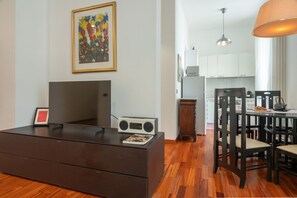 A modern living room with a flat-screen TV, a radio, a framed artwork, and a dining area with wooden chairs and a table. - Casa Novecento Prati (Roma)
