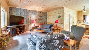 Een gezellig blokhutinterieur met een woonkamer, inclusief een bank, fauteuil en een televisie.