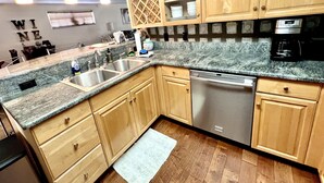 A kitchen with wooden cabinets, granite countertops, a dishwasher, and a coffee maker. - Cozy beach home! Private pool, 2min walk to beach, walkable to restaurants/shops (New Smyrna Beach)
