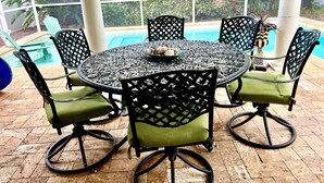A round table with six chairs, each with a green cushion, set on a tiled floor. - Cozy beach home! Private pool, 2min walk to beach, walkable to restaurants/shops (New Smyrna Beach)