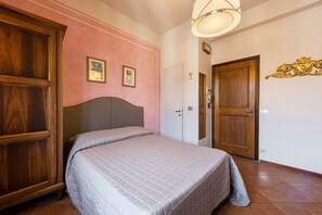 Une chambre à coucher avec un lit, une armoire en bois, deux tableaux encadrés accrochés au mur, une porte et un luminaire.