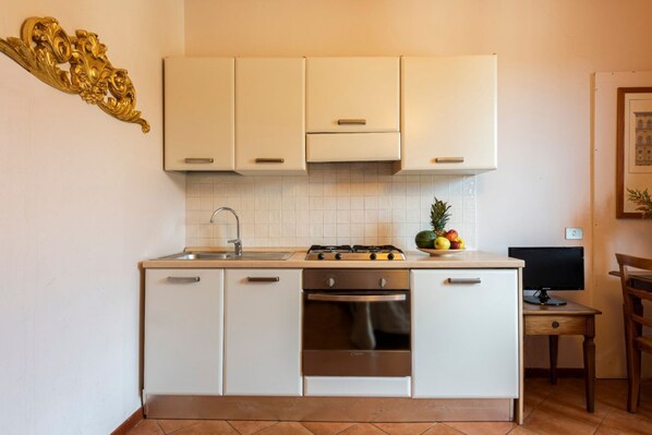 Une cuisine avec des meubles blancs, une cuisinière, un four, un évier et une petite table sur laquelle se trouve un ordinateur.