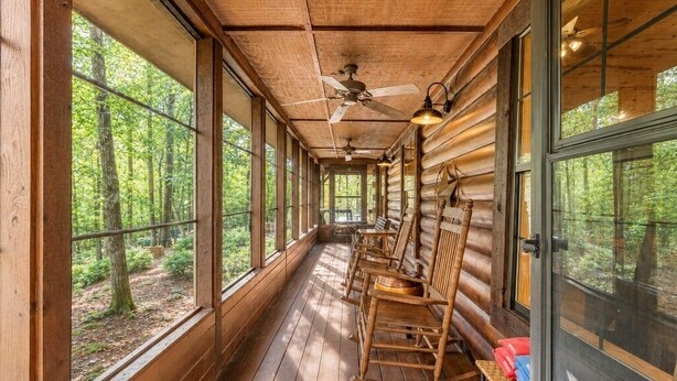 A log cabin with a porch, wooden rocking chairs, and large windows offering forest views.