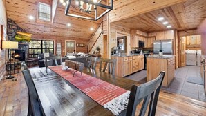 A spacious wooden cabin with a dining area, kitchen, and a fireplace.