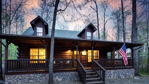 A log cabin with a stone foundation, wooden porch, and a flag.