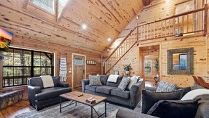 A spacious wooden cabin interior with two sofas, a coffee table, and a staircase leading to an upper level.