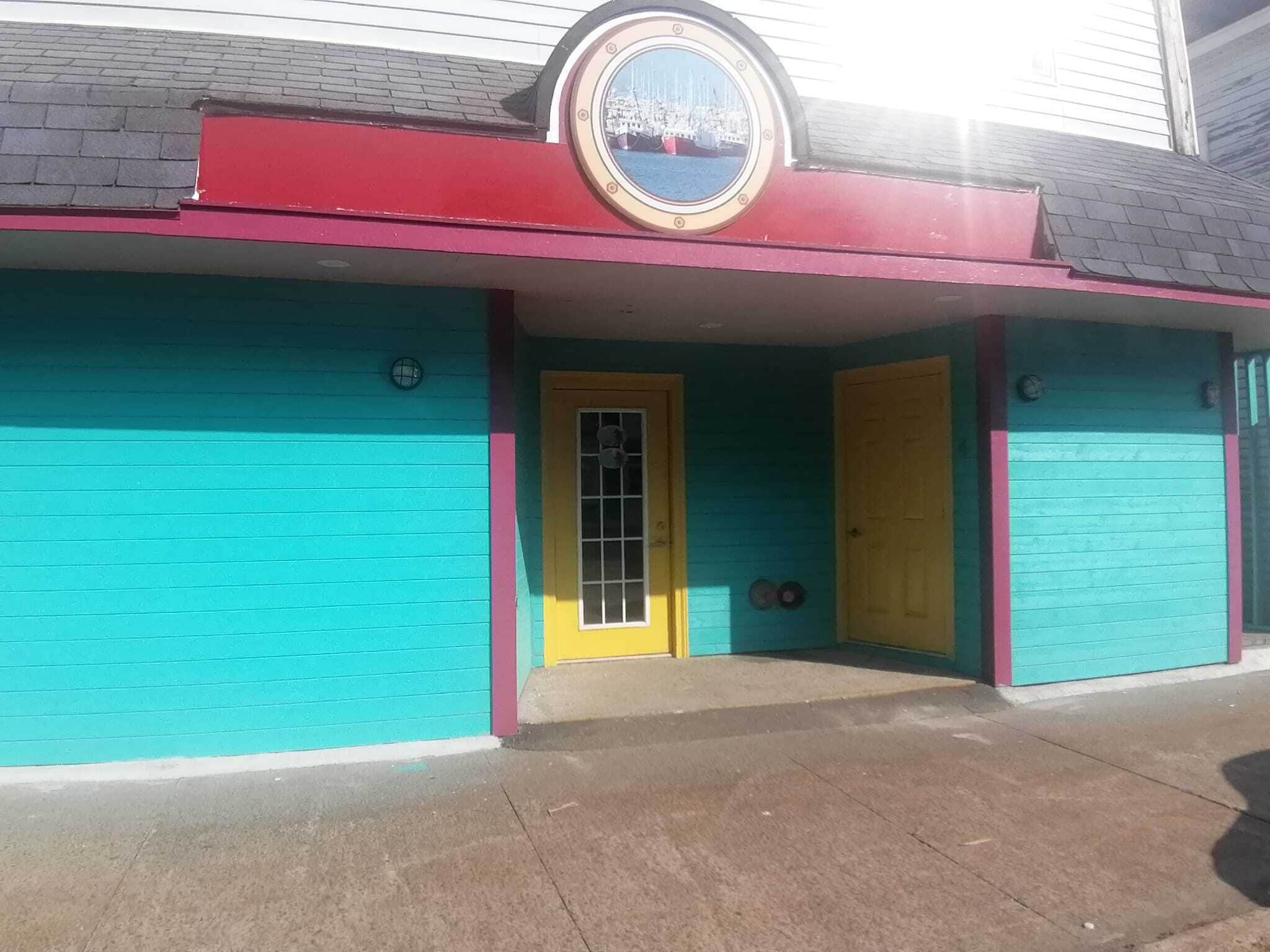 A building with a turquoise facade, a yellow door, and a small window with a metal grid.