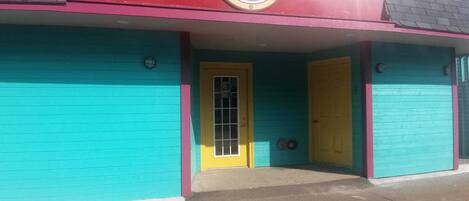 A building with a turquoise facade, a yellow door, and a small window with a metal grid.