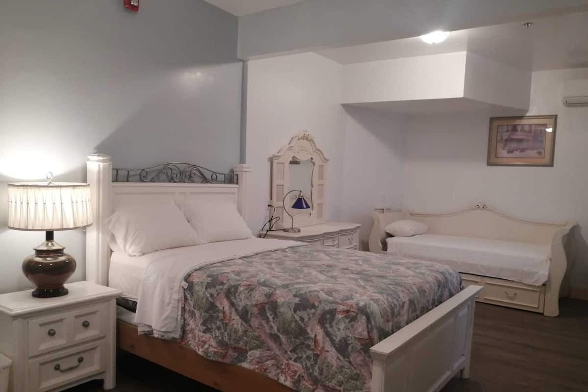 A bedroom with a bed, a nightstand, a dresser, a mirror, and a bedside table.
