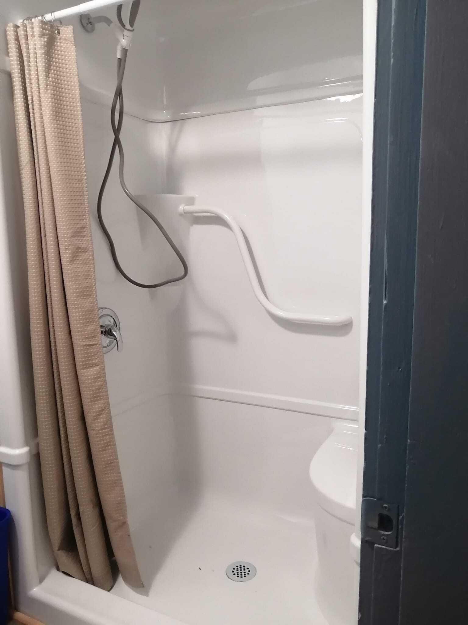 Un box de ducha con cortina color beige, pared blanca y suelo blanco.