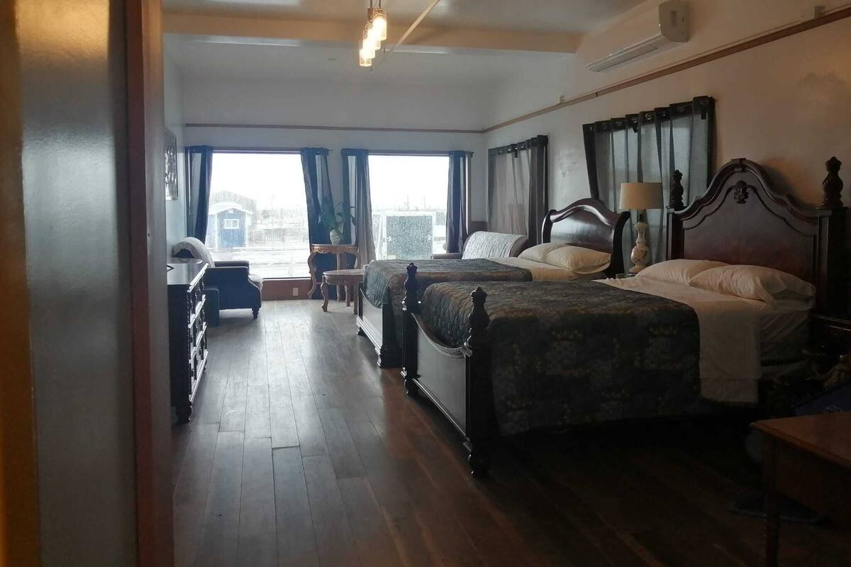 A hotel room with two beds, a wooden floor, a window with curtains, and a ceiling light.