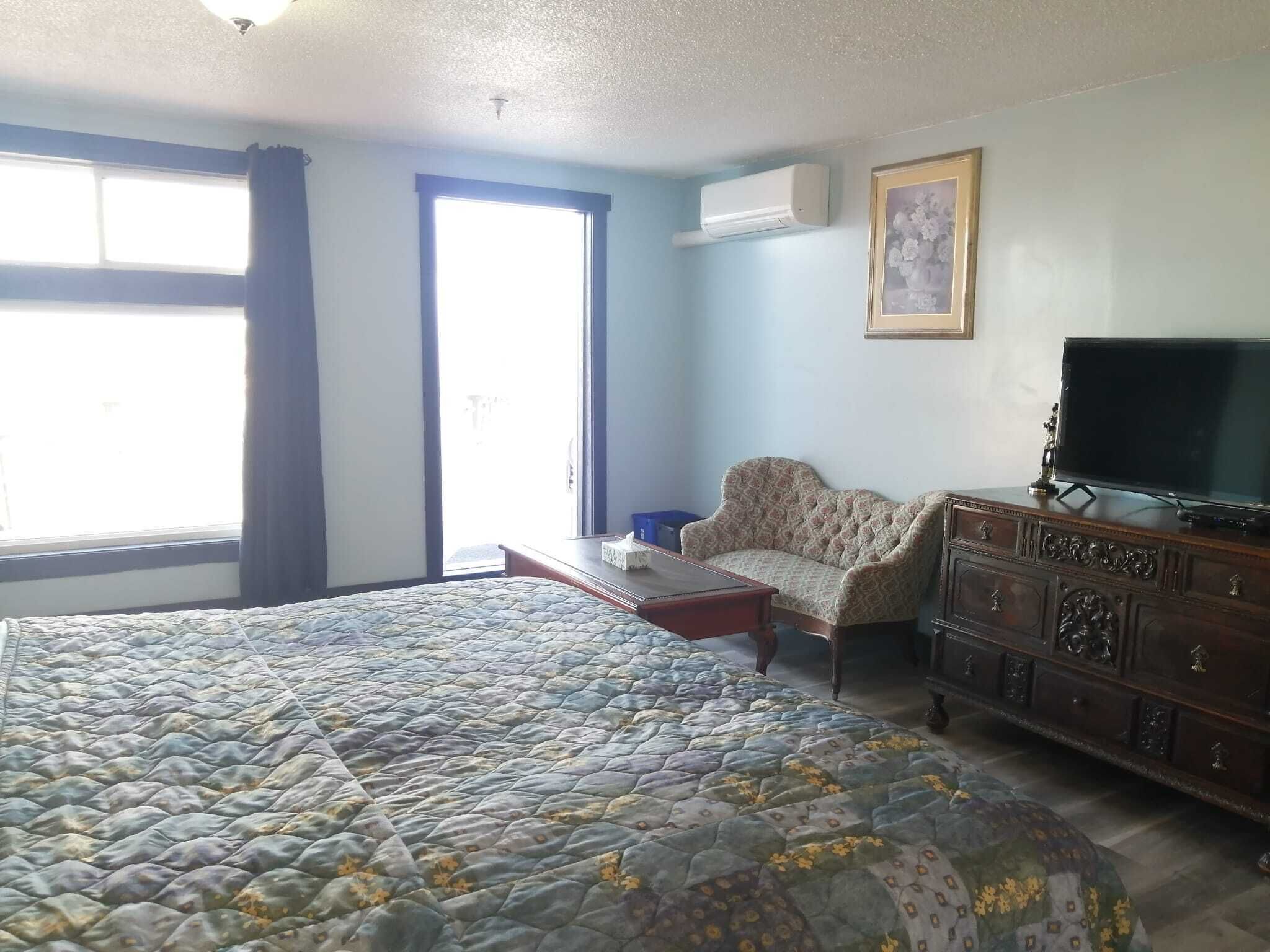 A bedroom with a large bed, a dresser, a television, and a window with curtains.