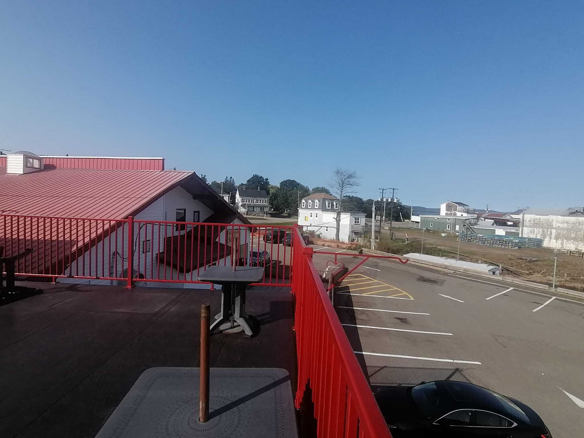 A parking lot with a red fence, a building with a red roof, and a clear blue sky.