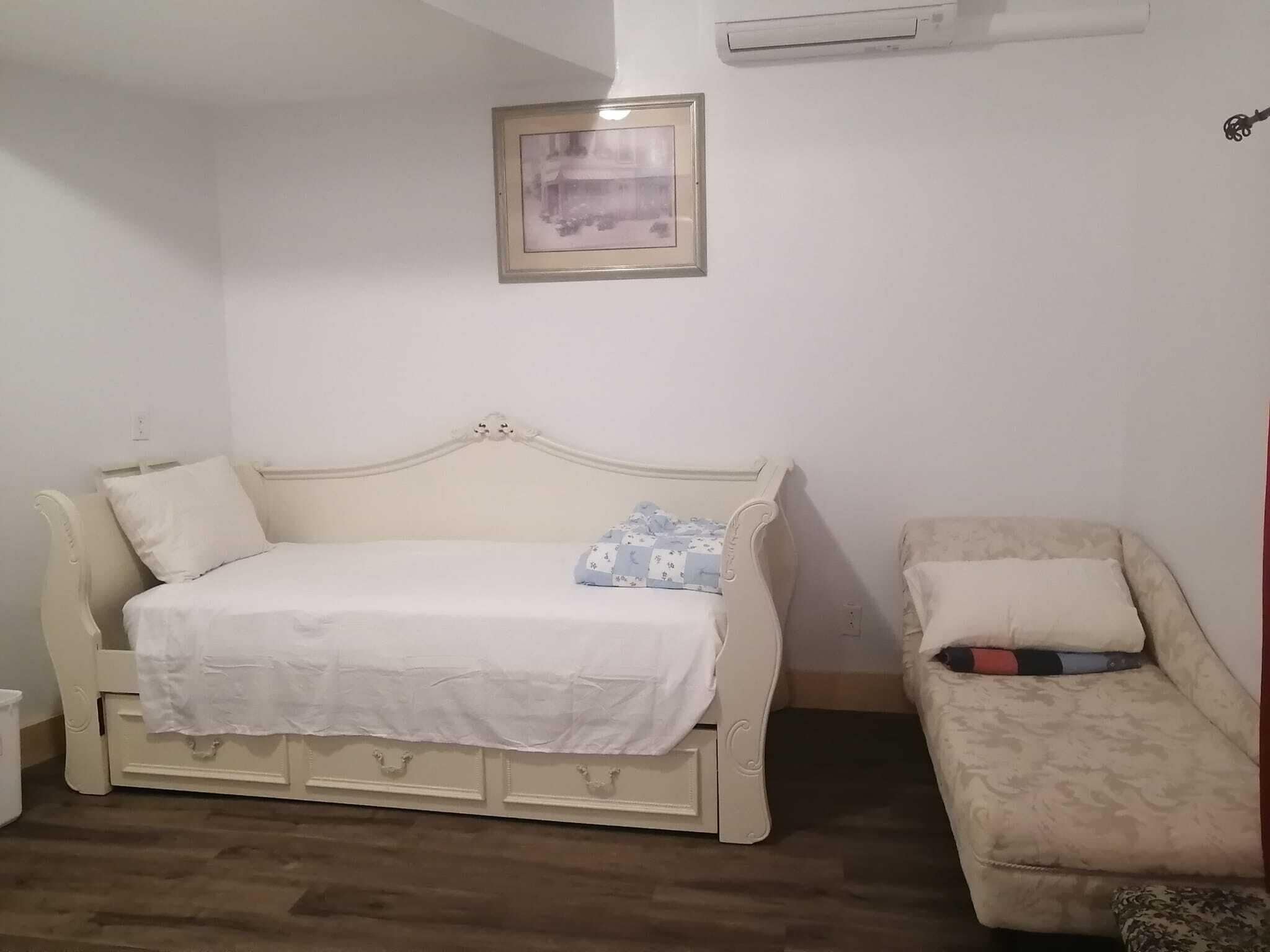 A room with a white bed, a white sofa, a small table, and a framed picture on the wall.
