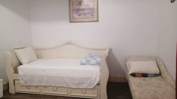 A room with a white bed, a white sofa, a small table, and a framed picture on the wall.