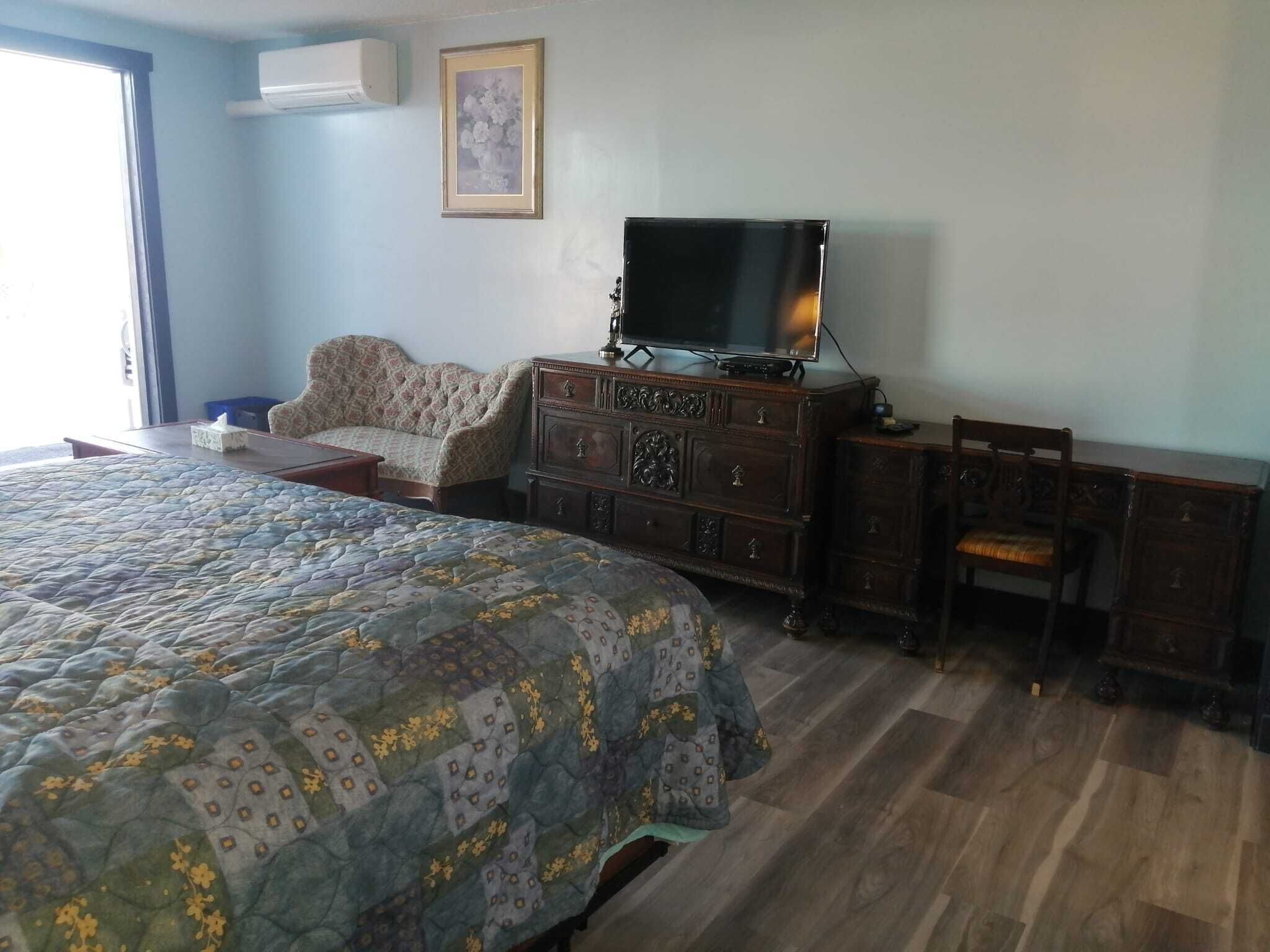 A bedroom with a large bed, a dresser, a television, and a chair.