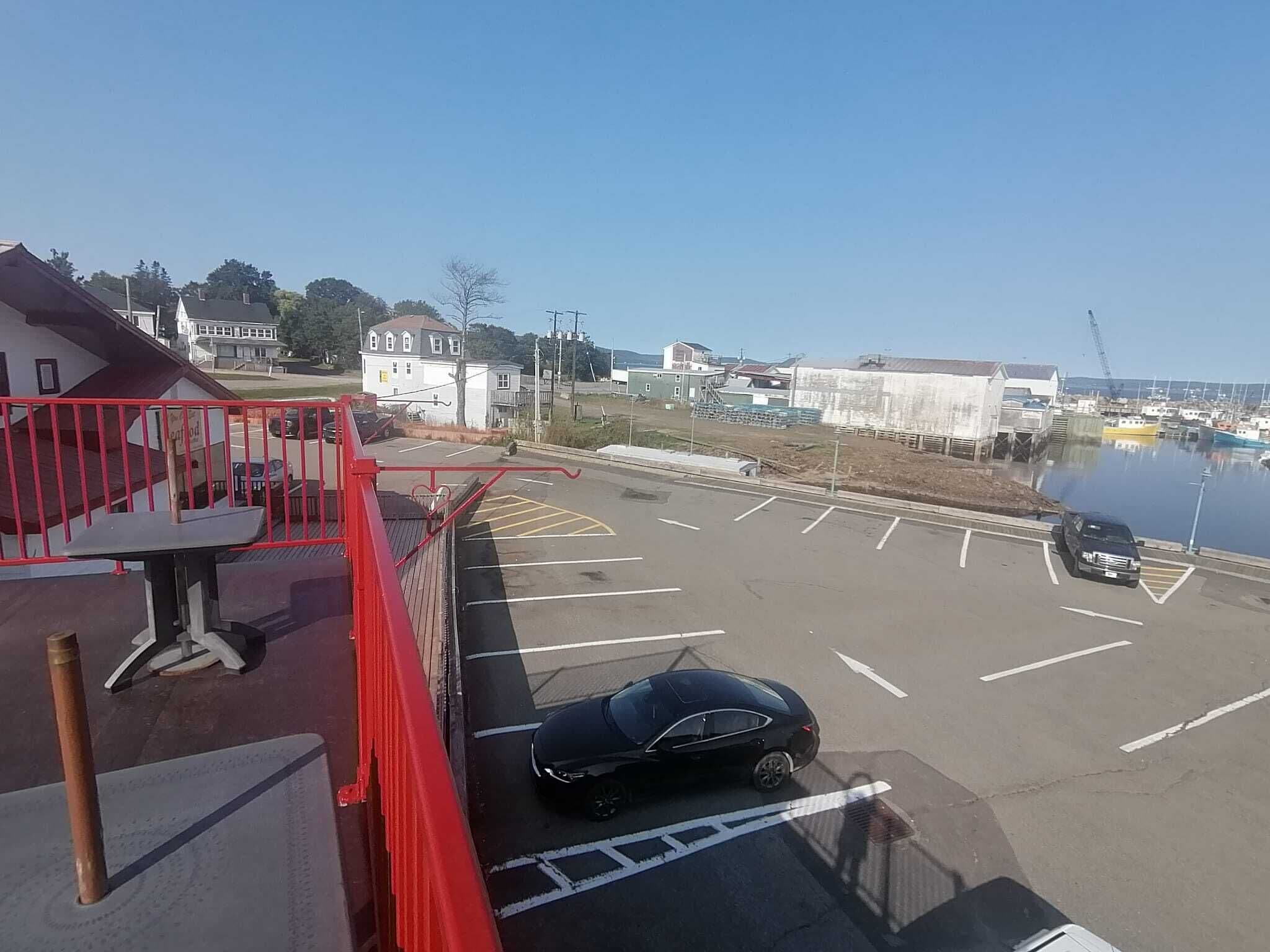 A parking lot with a black car, a red railing, and a view of a marina with boats.