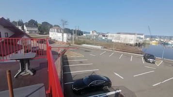 A parking lot with a black car, a red railing, and a view of a marina with boats.