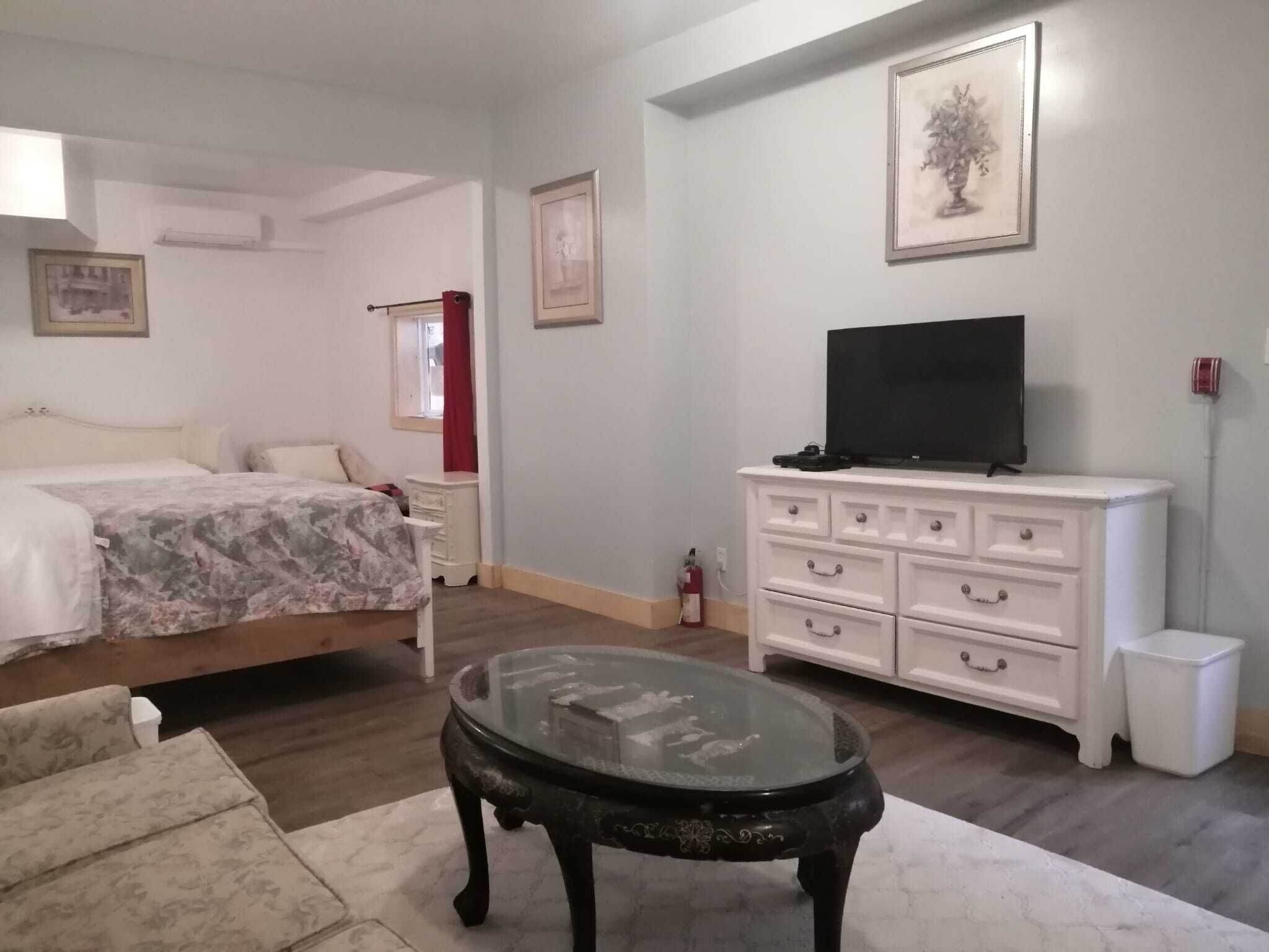 A bedroom with a bed, a dresser, a TV, and a glass table.