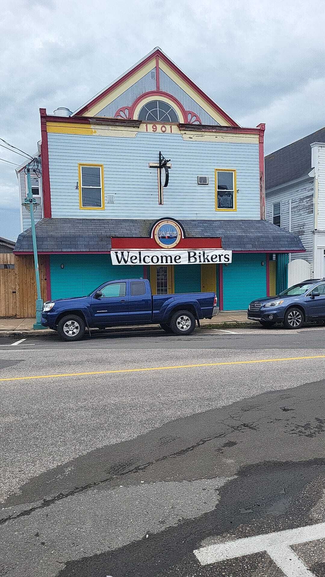 A building with a 'Welcome Bikers' sign, a blue truck parked in front, and a garage door.
