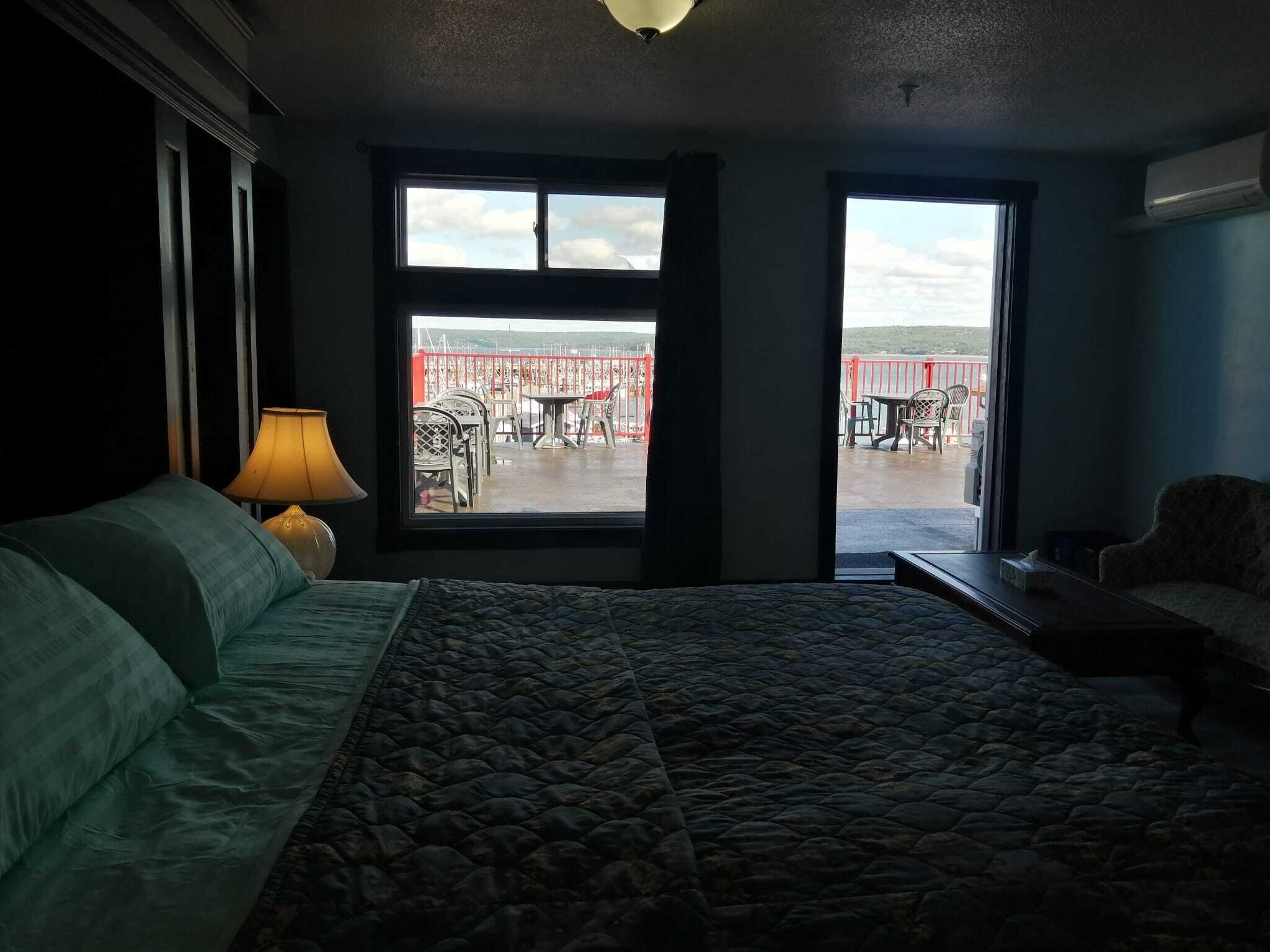 Una habitación de hotel con cama, lámpara y vista a un patio exterior con mesas y sillas.