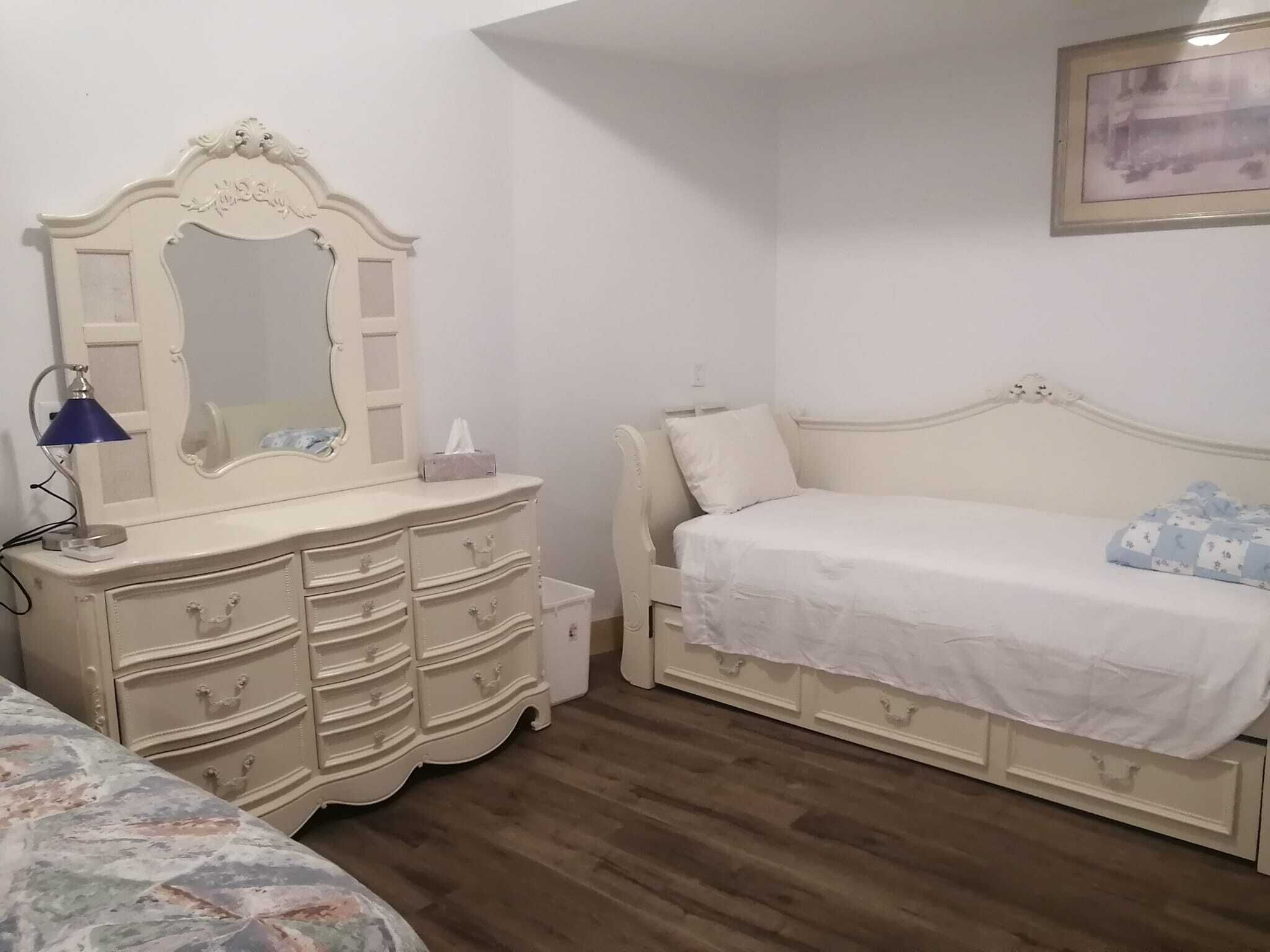 Een slaapkamer met een bed, een dressoir, een spiegel en een nachtkastje.