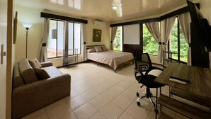 Una camera d'albergo con un letto, un divano, una scrivania con una sedia e ampie finestre con tende.