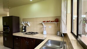 Una cucina con lavello in acciaio inossidabile, fornello, forno a microonde e macchina da caffè. Dispensa con tazze e frullatore.