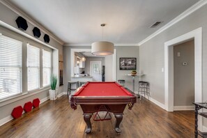 Relax in this spacious room with a pool table and dining area, featuring large windows and a kitchen counter.