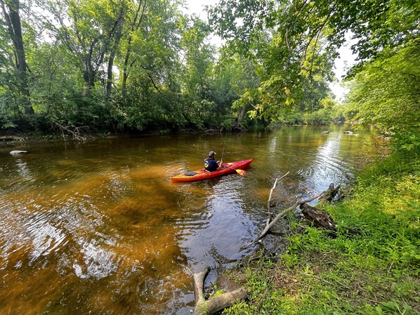 A person in a red kayak on a river surrounded by dense greenery. - Rustic Riverside A-Frame Retreat: Secluded Charm. (Racine)