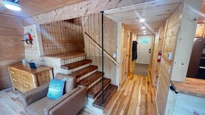 A wooden interior with a staircase, a sofa, and a kitchen area. - Rustic Riverside A-Frame Retreat: Secluded Charm. (Racine)