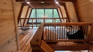 A wooden interior with a sloped ceiling, a wooden bench, and a view through a window. - Rustic Riverside A-Frame Retreat: Secluded Charm. (Racine)