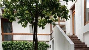 A courtyard with a tree, stone paving, a white building with a wooden staircase, and a wooden fence. - Suite Centro Histórico (Quito)